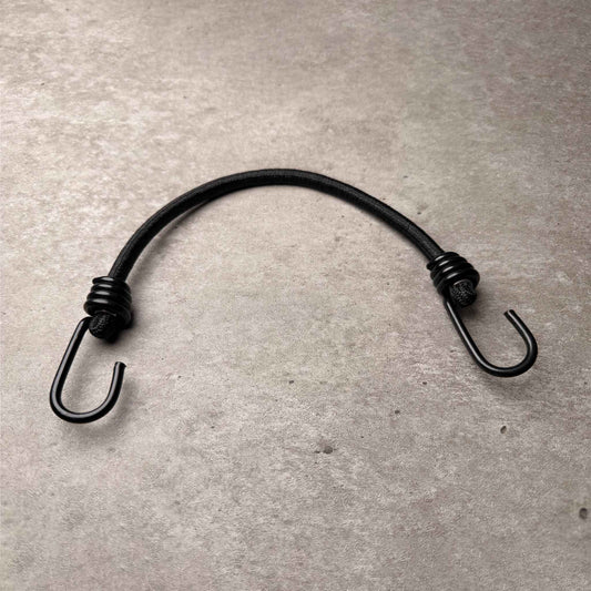 A black metal bungee hook with a textured wrap on both ends, resting on a textured gray concrete surface.