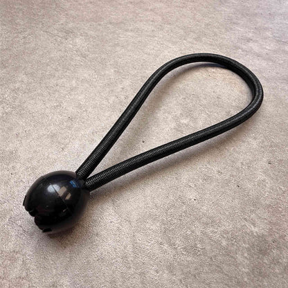 A black elasticated bungee ball loop, shown on a textured gray concrete surface.