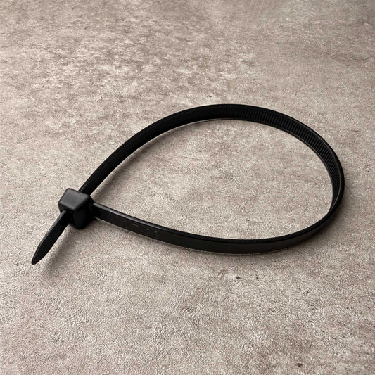 A single black plastic cable tie lying on a textured gray concrete surface.