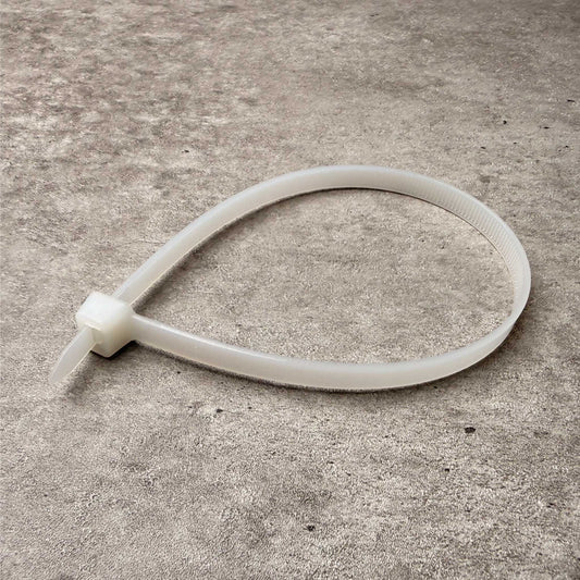 A translucent white plastic zip tie lying on a textured gray concrete surface.