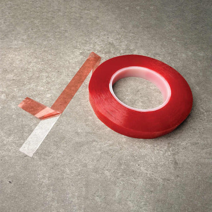 A roll of double sided adhesive tape with a strip peeled back, placed on a textured gray concrete surface.