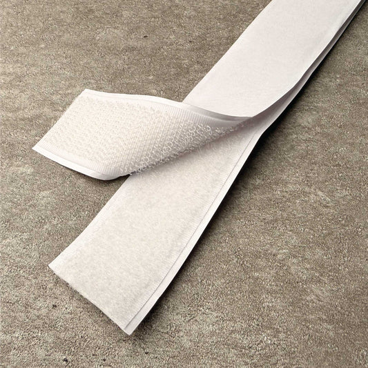 A close-up of velcro hook and loop being pulled apart, shown on a grey concrete surface.